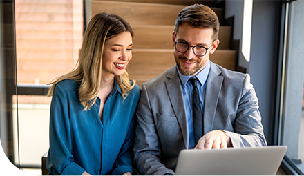 Casal analisa informações no notebook em ambiente corporativo.