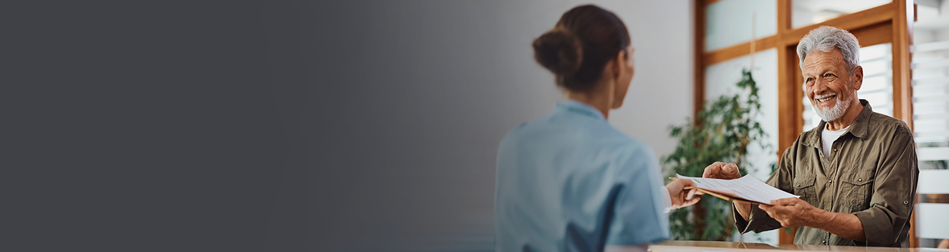 Idoso entregando documento para atendente em recepção de clínica médica.