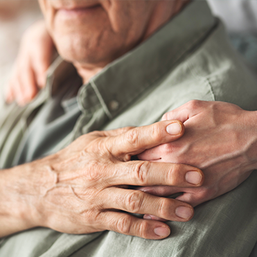 Mão de cuidador apoiando idoso em gesto de carinho e cuidado.